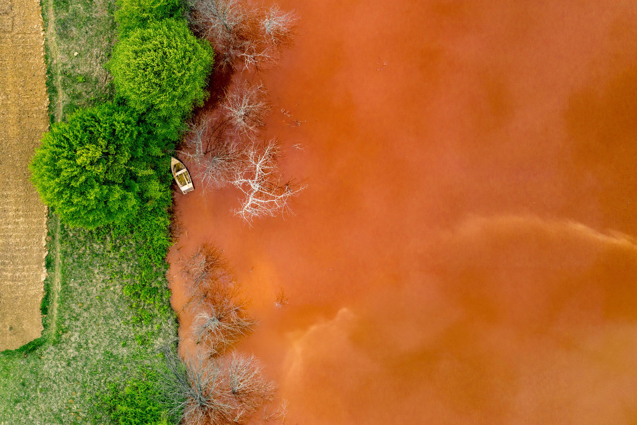 Drohnenaufnahme zeigt eine leuchtend rote Wasserfläche neben grünen Bäumen und Vegetation.