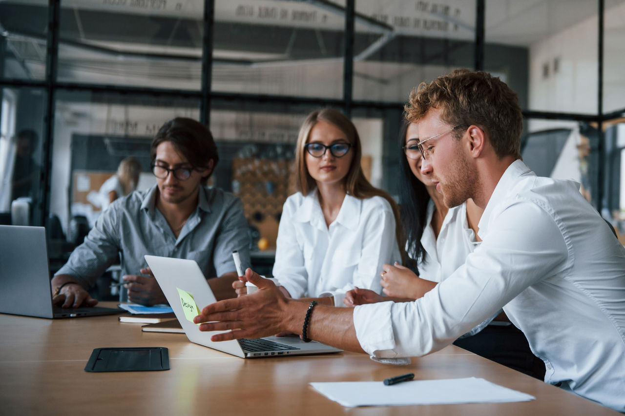 Kollegen diskutieren Projektideen, während sie Inhalte auf einem Laptop in einem Konferenzraum überprüfen.