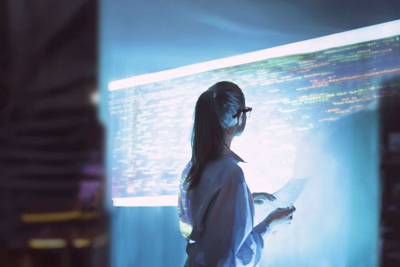 IT‑Expertin analysiert Code und Daten auf großem digitalen Display in moderner Arbeitsumgebung