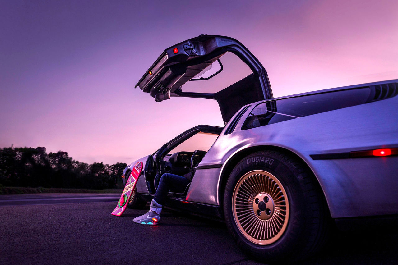 Sportwagen mit geöffneten Flügeltüren im Abendlicht, daneben steht ein schwebendes Hoverboard auf der Straße.
