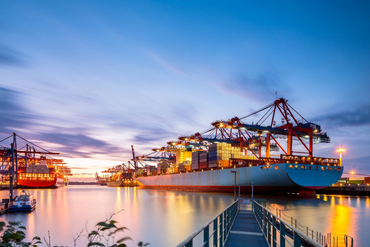 Containerhafen bei Sonnenuntergang mit Frachtschiffen und Kränen, Symbol für globale Logistik und Handel.