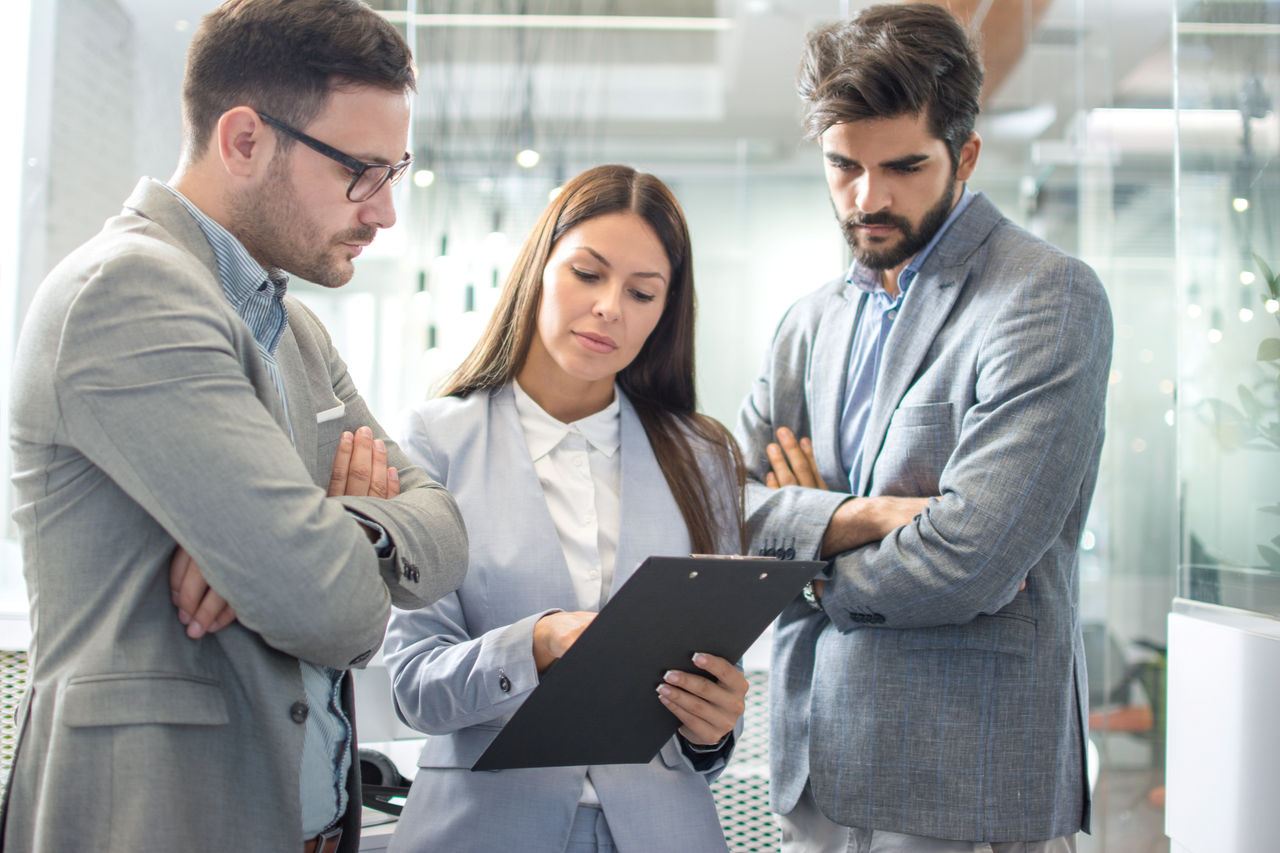 Drei Fachkräfte prüfen Unterlagen und besprechen Geschäftsthemen in einem modernen Büro.