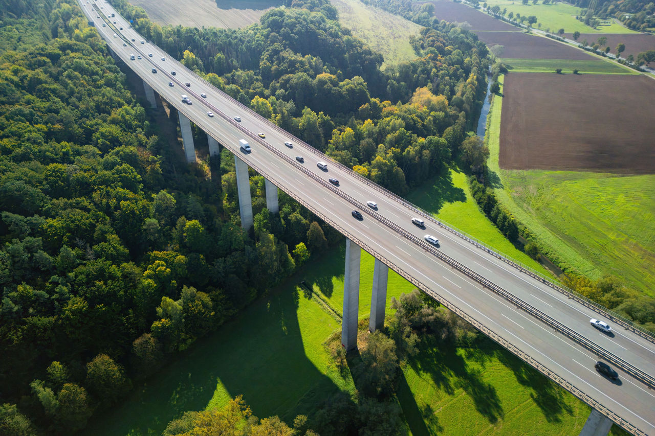Autobahnbrücke über bewaldetes Tal mit fließendem Verkehr, umgeben von Feldern und grüner Landschaft.