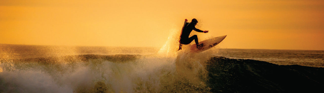 Dynamische Surfaufnahme mit springender Person auf einer Welle bei goldenem Sonnenlicht.