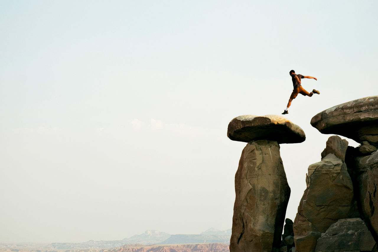 Ein junger Mann springt über eine Reihe von Felsen in der Wüstenlandschaft von Moab, Utah.