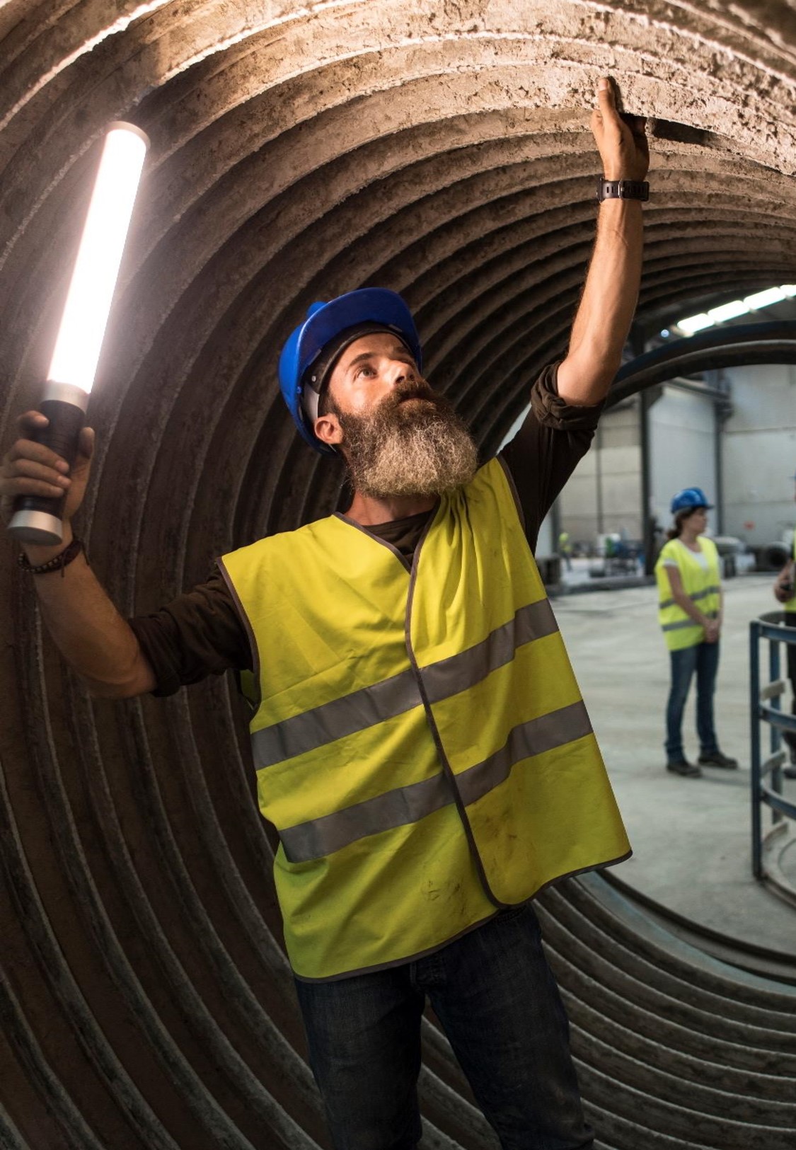 Arbeiter mit Lampe prüft große Röhrenstruktur.