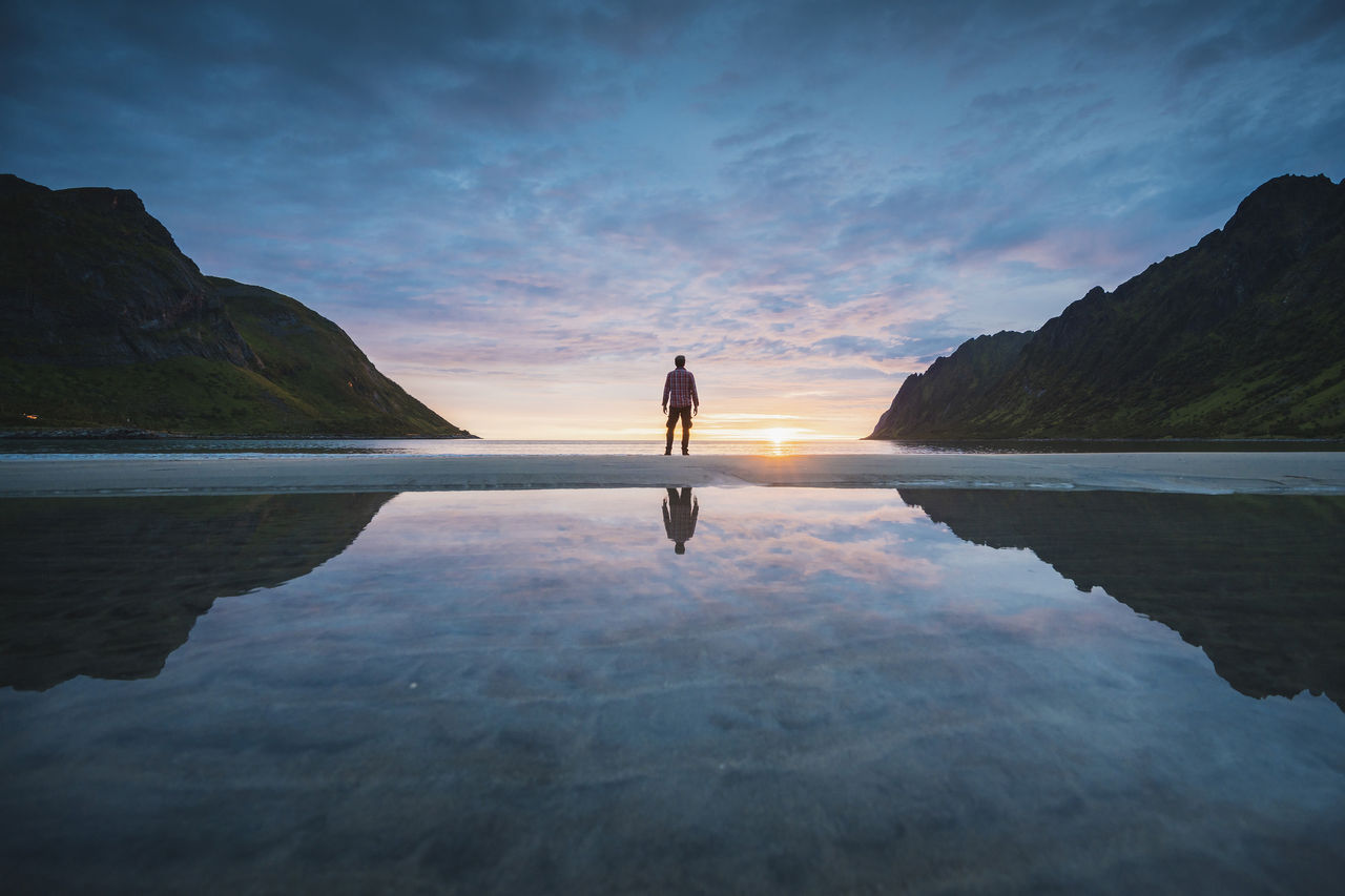 Person standing on a serene beach with reflection during stunning sunset