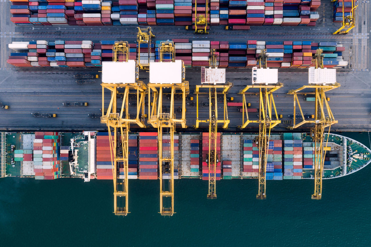 Top-down view of a container terminal showing gantry cranes, stacked cargo containers, and docked ships.