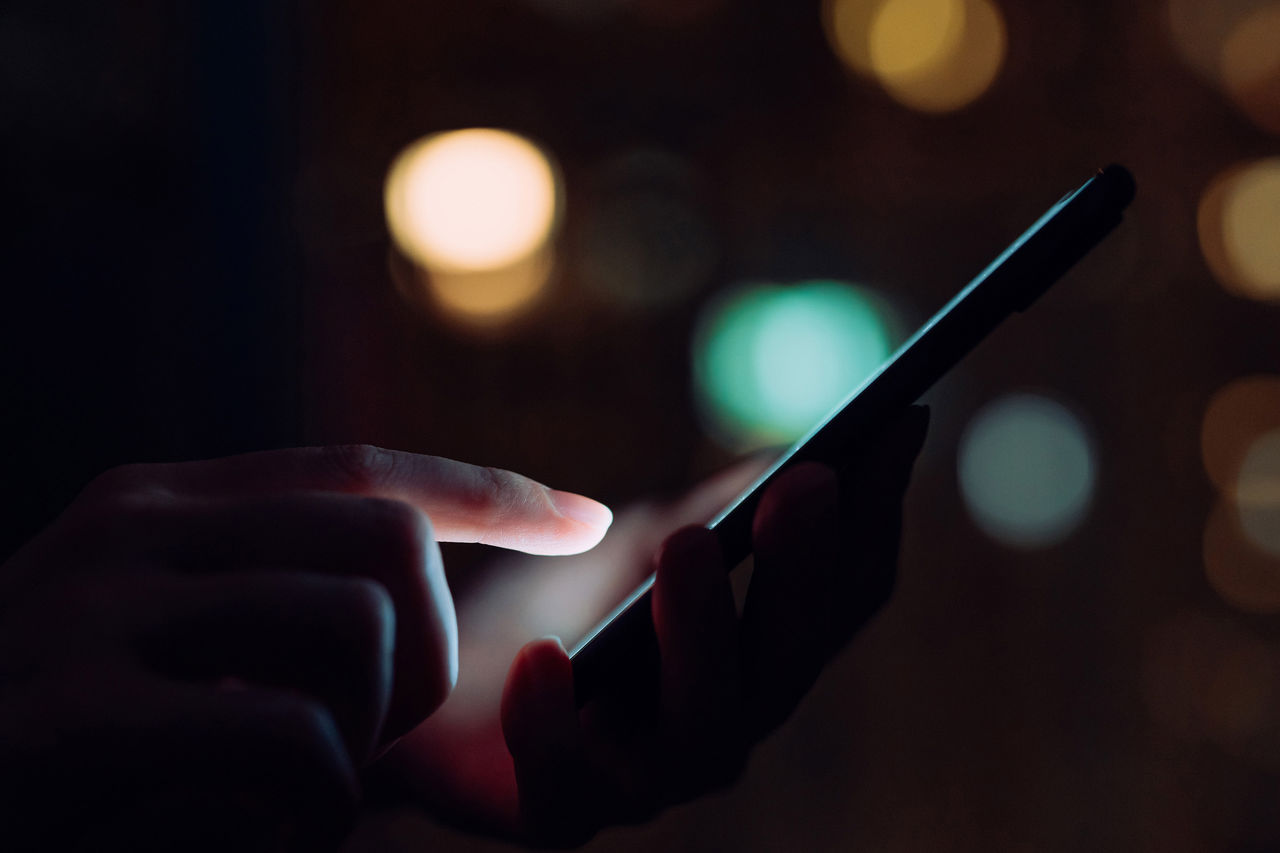 Close up of woman's hand using smartphone in the dark, against illuminated city light bokeh