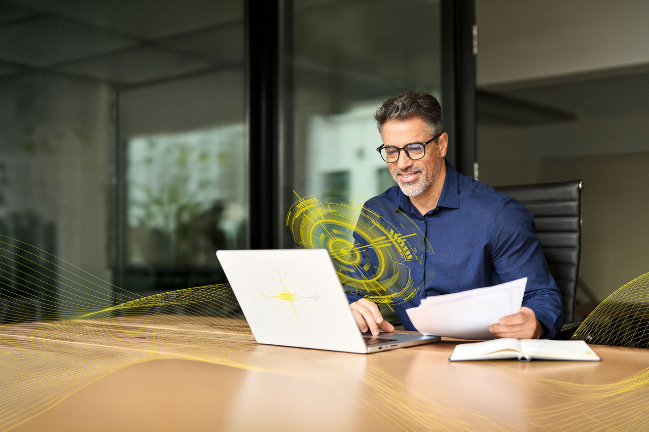 Happy busy older business man using laptop looking at document in office