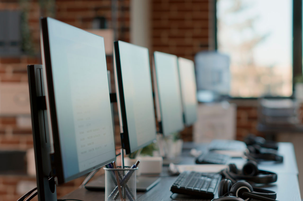 Nobody at customer care workstation with multiple computers used by telemarketing agents to give support to clients at call center helpline. Empty desks with monitors and headphones.