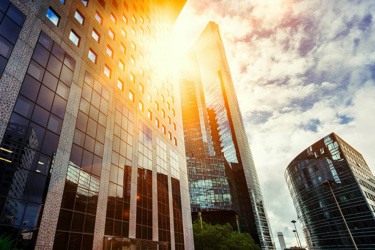 Skyscraper glass facades on a bright sunny day with sunbeams in the blue sky. Modern buildings in business district. Economy, finances, business activity concept. Bottom up view