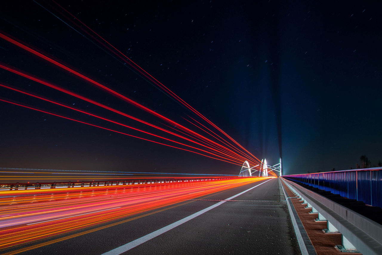 light traces of cars driving along the road at night through a beautiful modern highway bridge